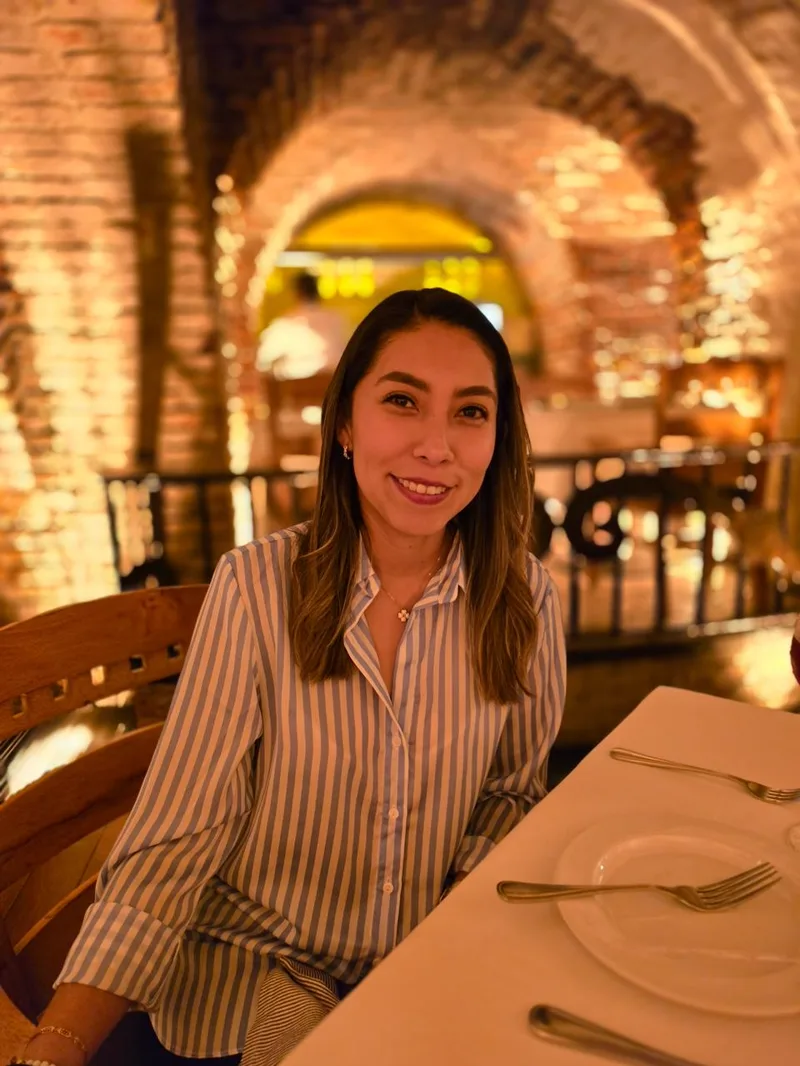 Retrato de Sandy sonriendo, en un salón de bóvedas de ladrillo