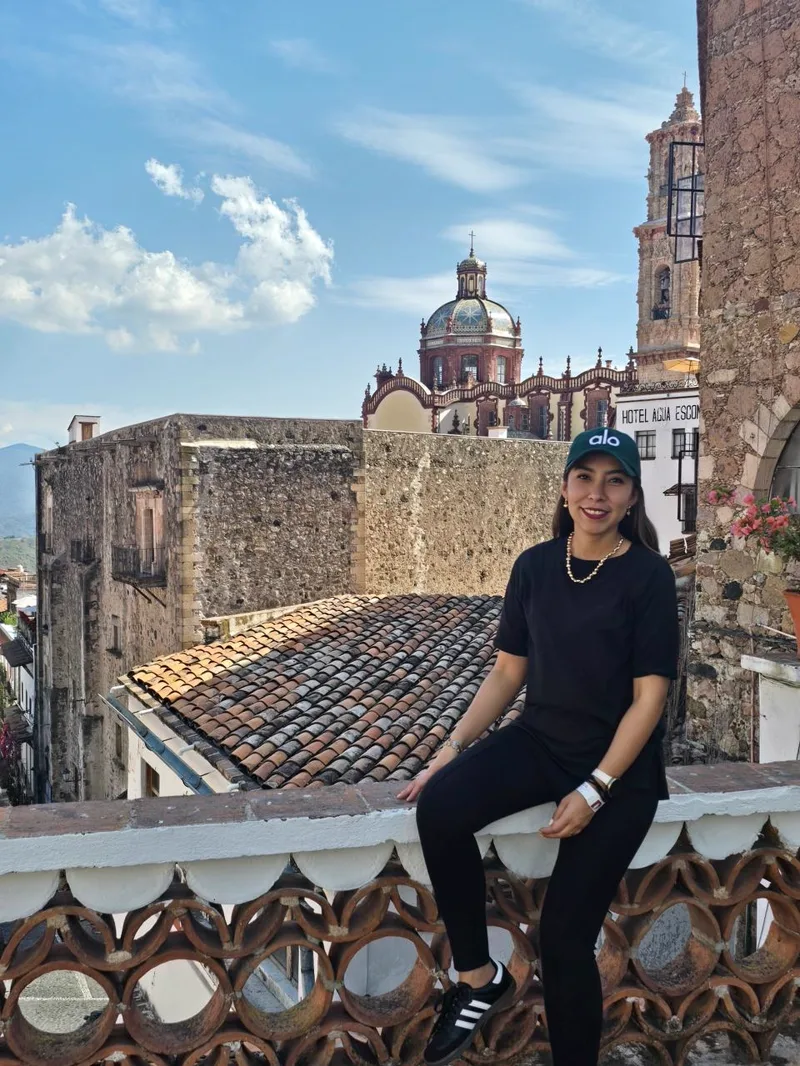 Sandy en Taxco, sentada en un pretil con la iglesia de Santa Prisca al fondo