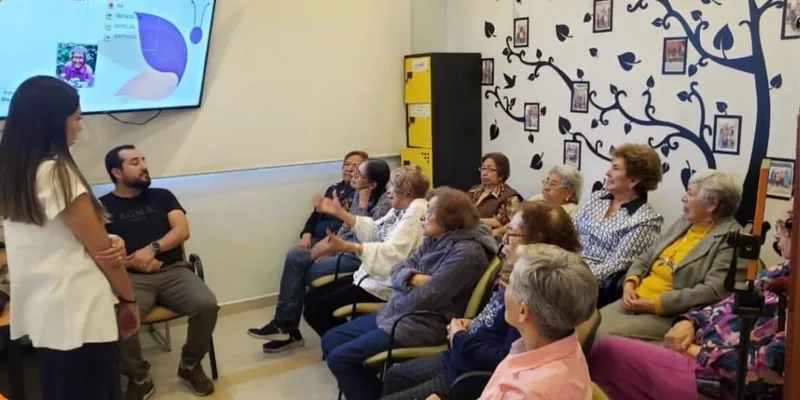 Plano abierto del taller de tanatología y proceso de duelo, con Sandy de pie frente al grupo
